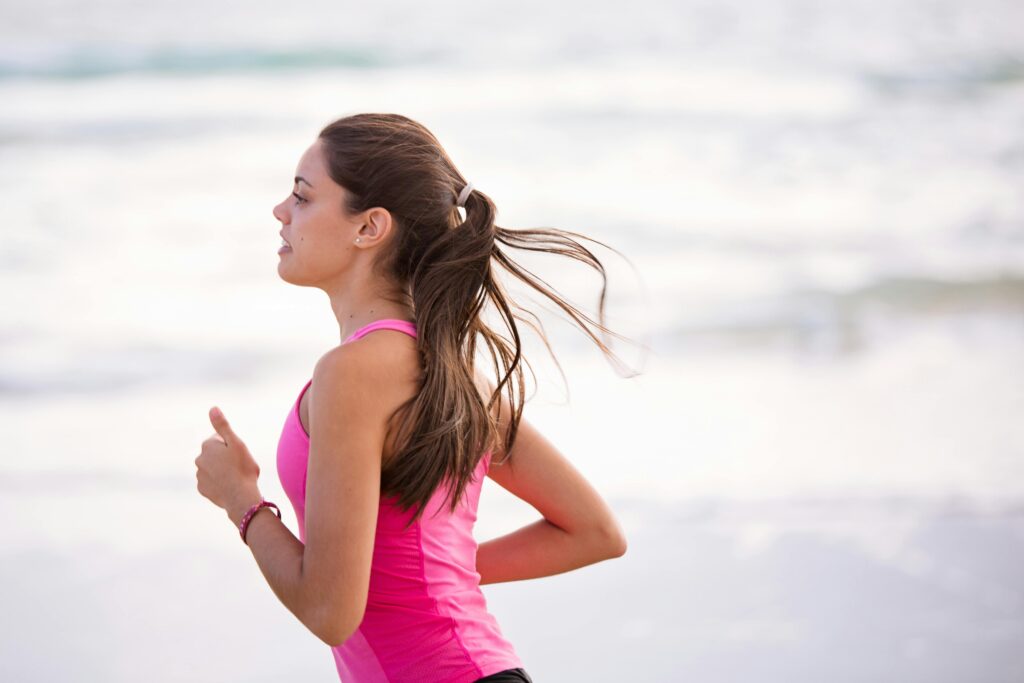 woman with brown hair and pink top running at the beach