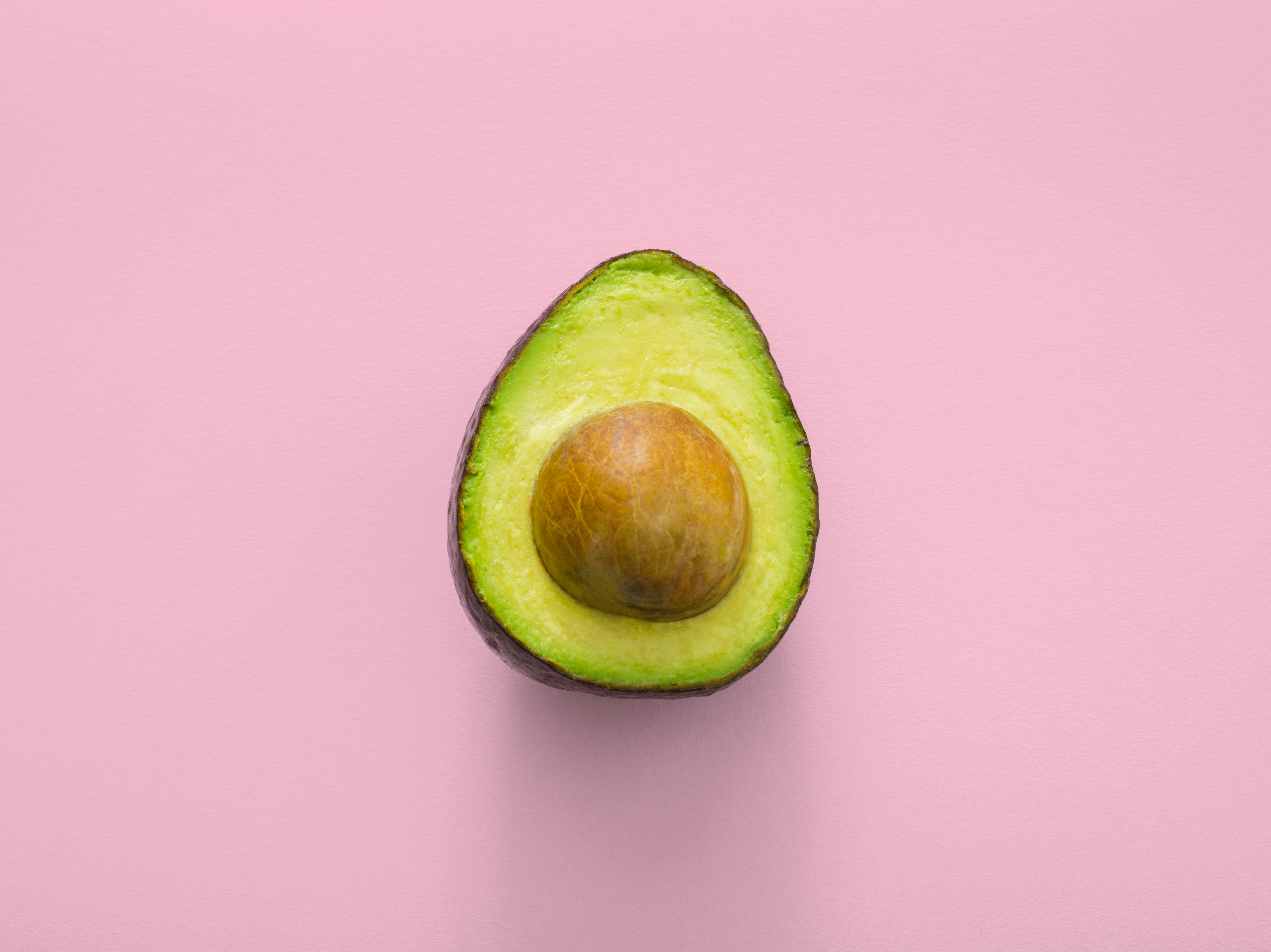 sliced avocado with stone in front of pink background