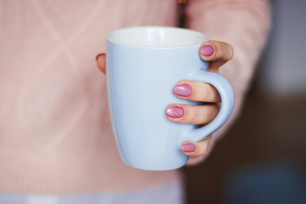 woman with nail polish holding cup of warm coffee or tea